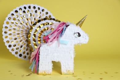 Photo of Unicorn shaped pinata and party decor on yellow background