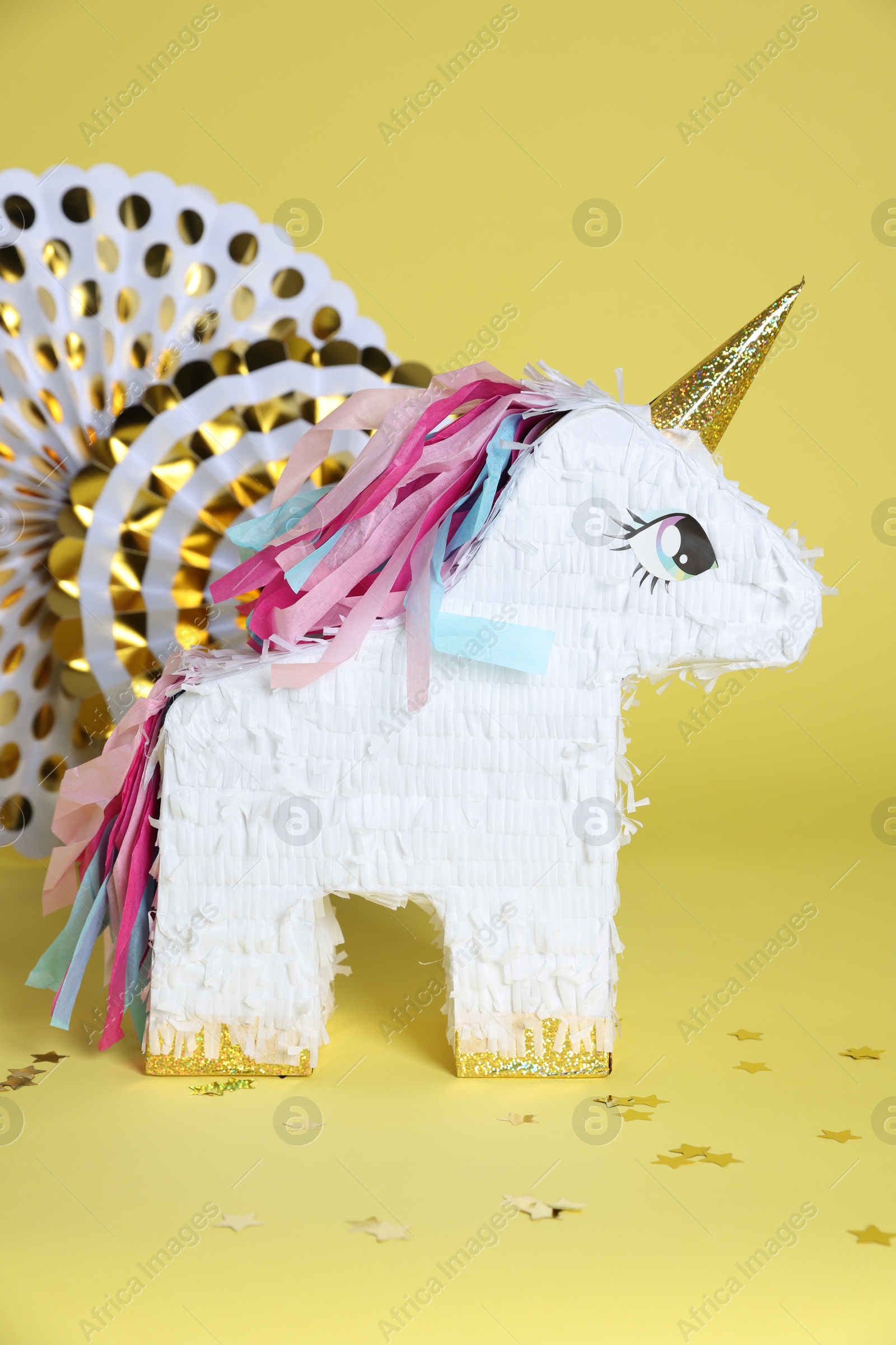 Photo of Unicorn shaped pinata and party decor on yellow background