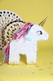 Photo of Unicorn shaped pinata and party decor on yellow background