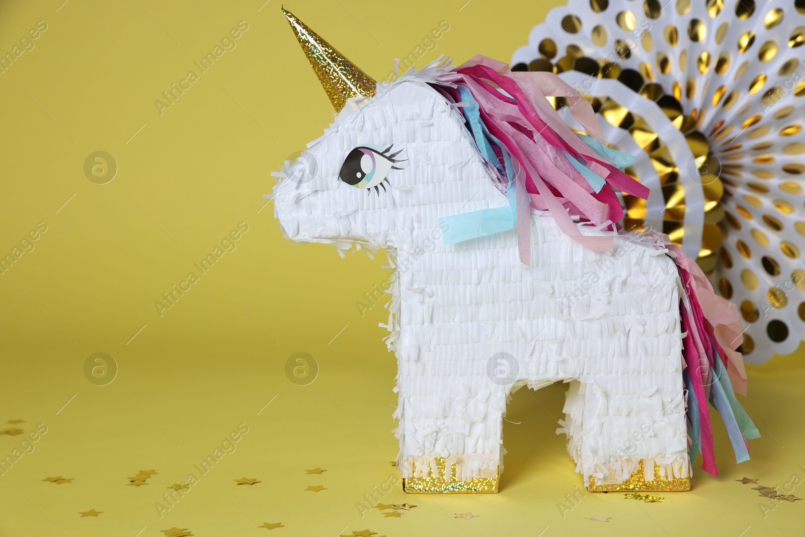 Photo of Unicorn shaped pinata and party decor on yellow background, space for text