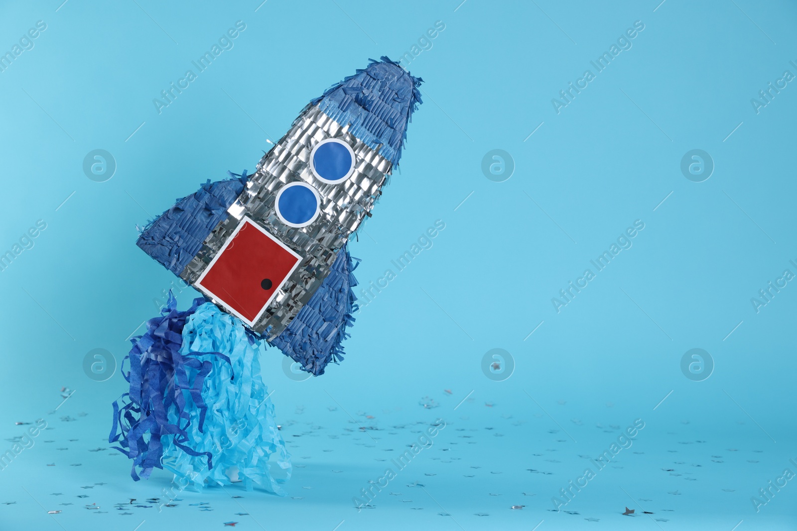 Photo of Rocket shaped pinata and confetti on light blue background, space for text