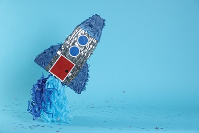 Photo of Rocket shaped pinata and confetti on light blue background, space for text