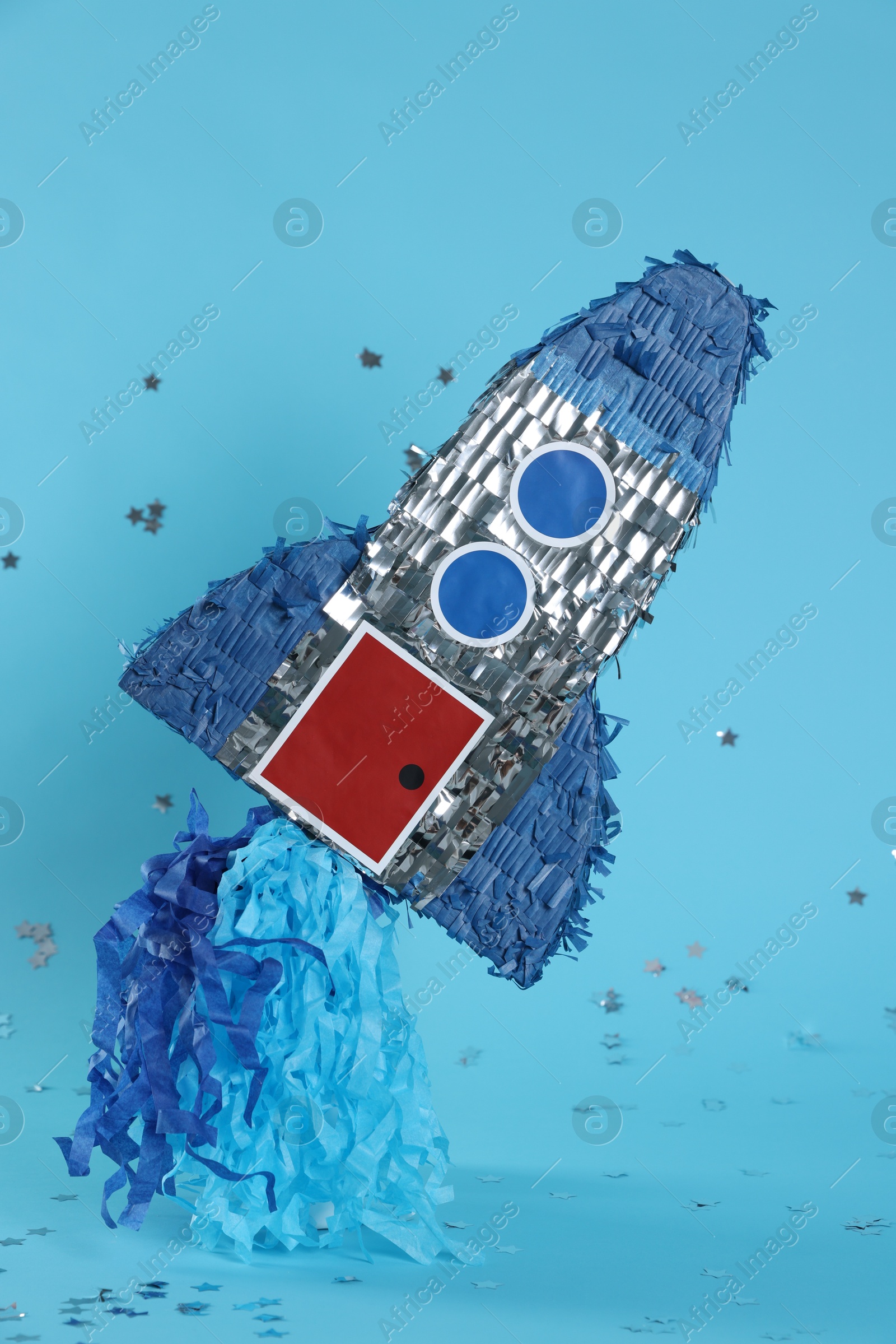 Photo of Rocket shaped pinata and confetti on light blue background