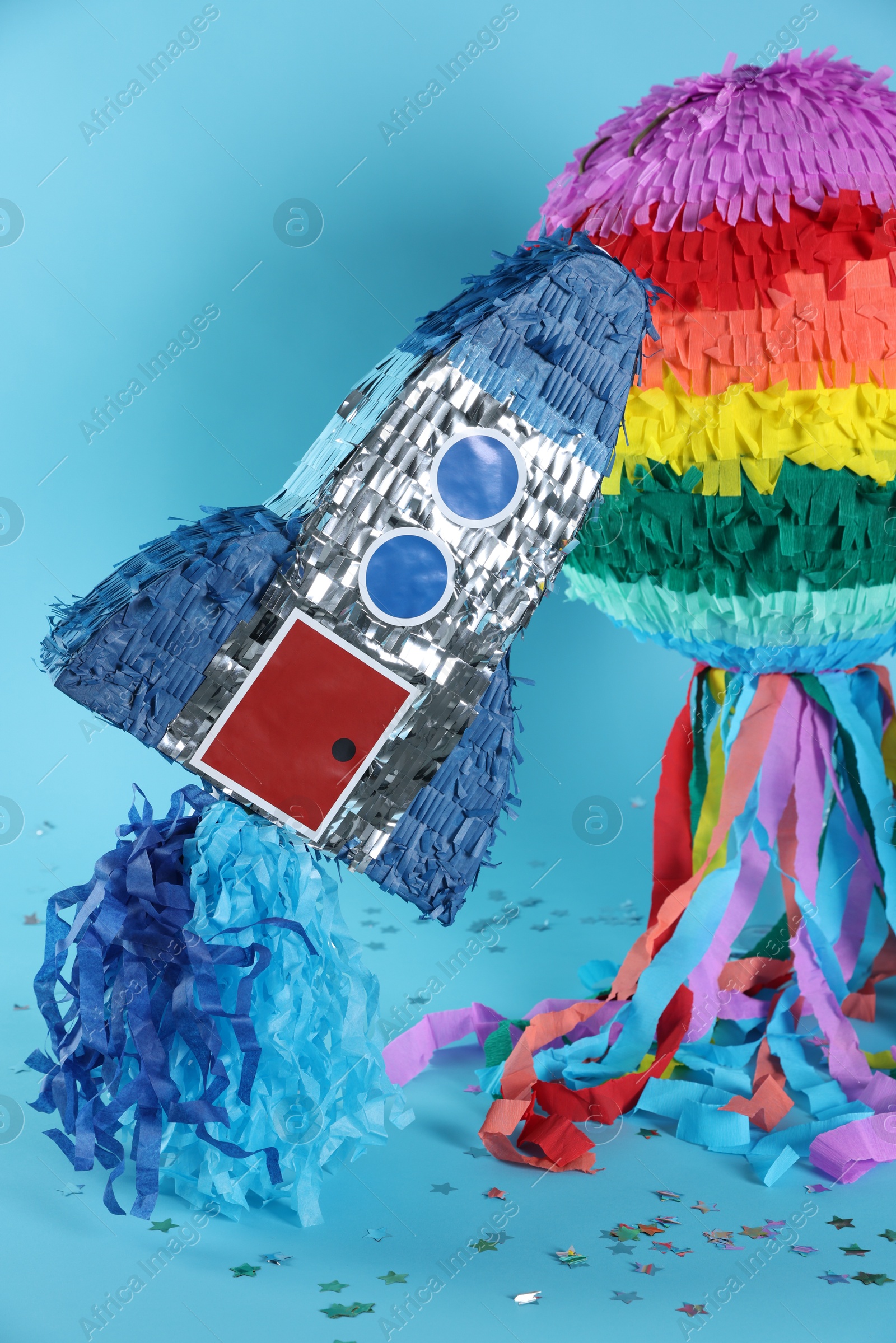 Photo of Bright colorful pinatas and confetti on light blue background