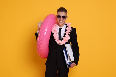 Photo of Businessman with folders, wreath of flowers and inflatable ring on orange background