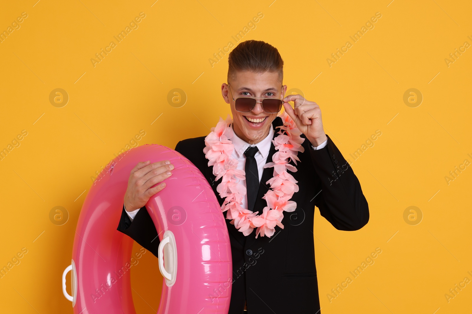 Photo of Businessman with wreath of flowers and inflatable ring on orange background