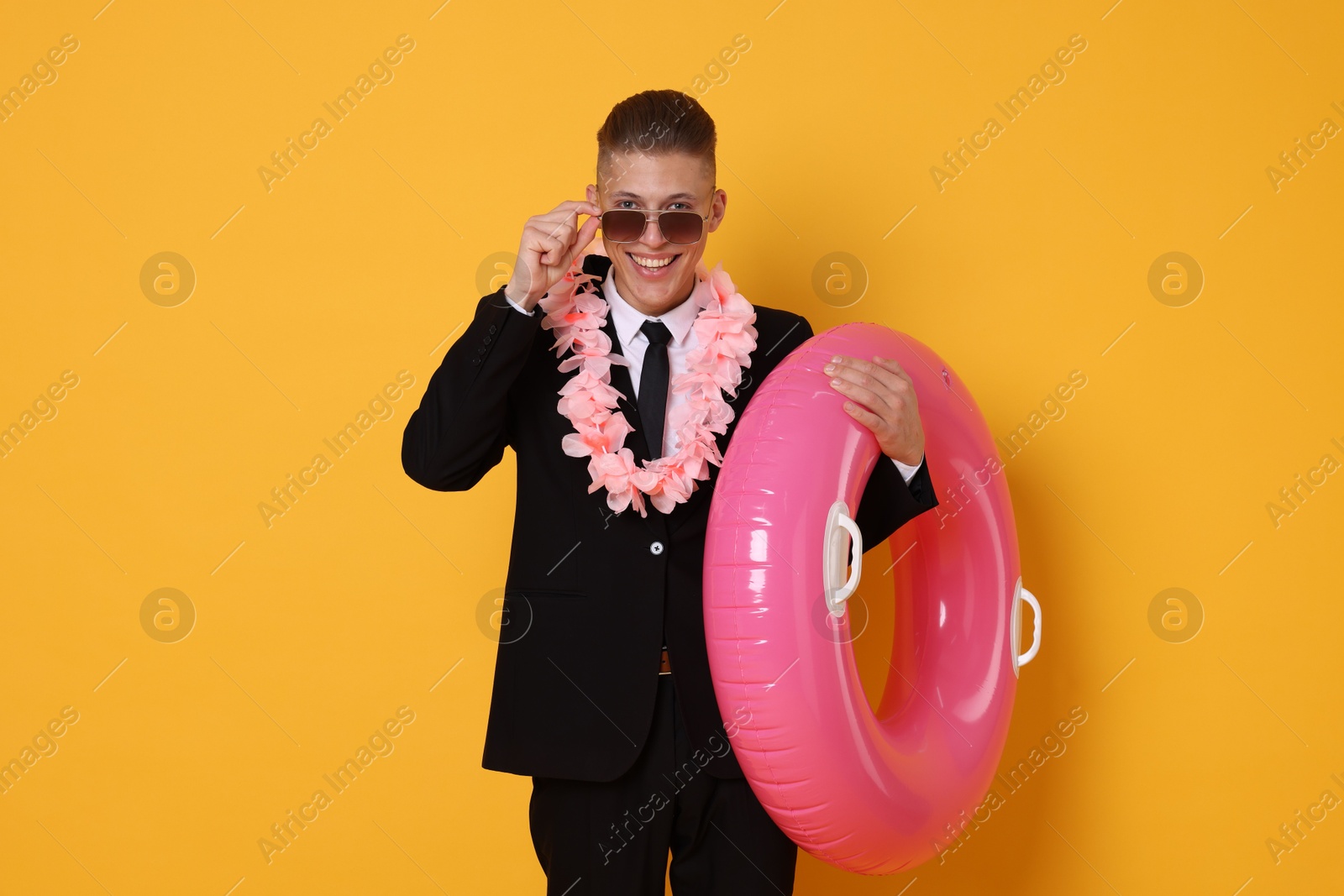 Photo of Businessman with wreath of flowers and inflatable ring on orange background