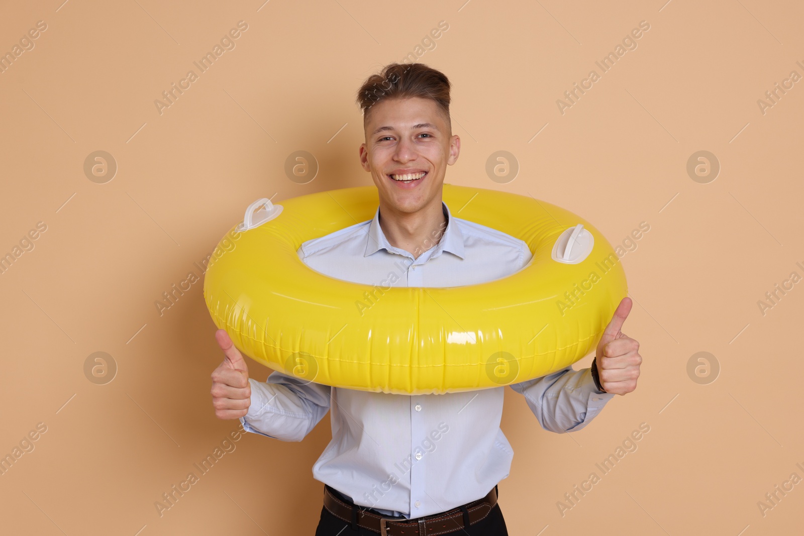 Photo of Businessman with inflatable ring showing thumbs up on beige background