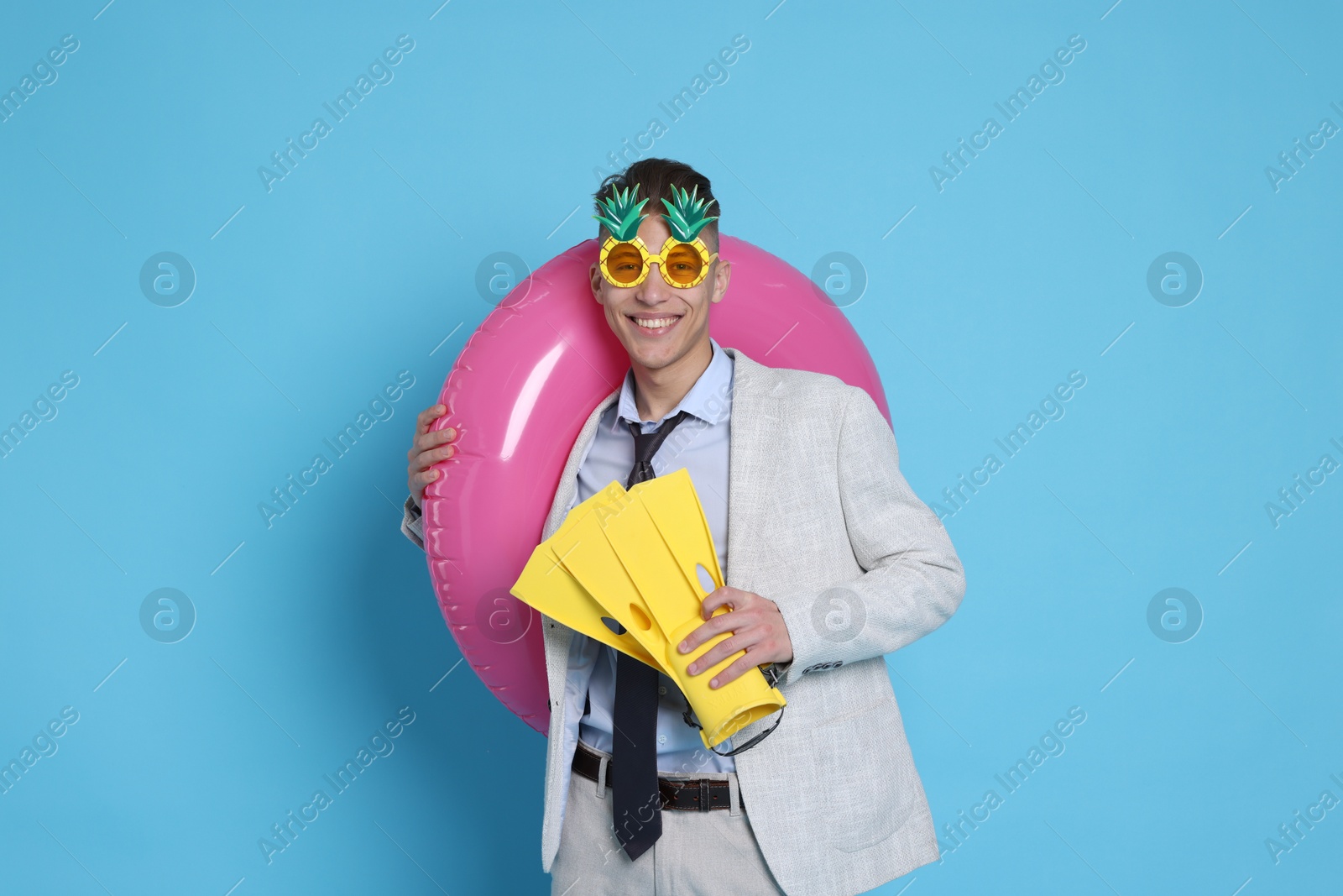 Photo of Businessman with inflatable ring, funny sunglasses and flippers on light blue background