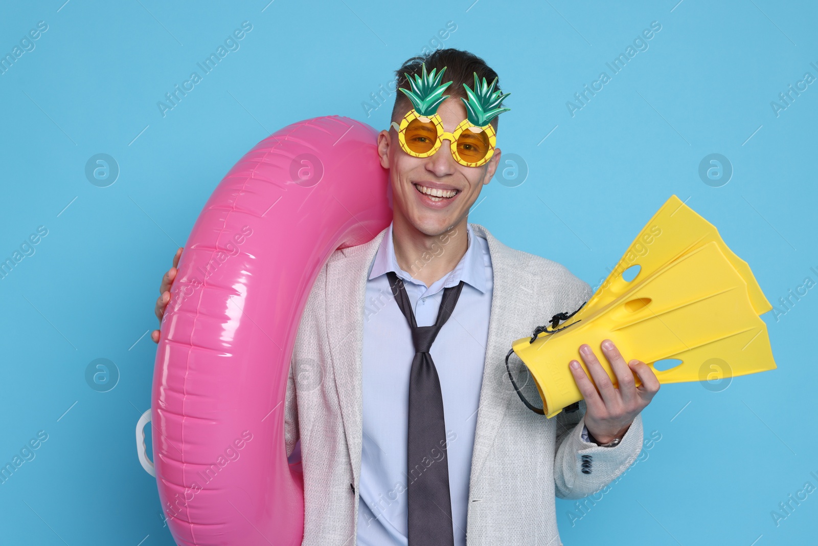 Photo of Businessman with inflatable ring, funny sunglasses and flippers on light blue background