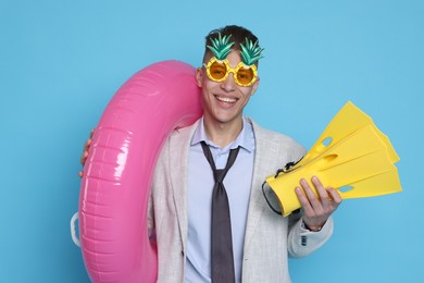 Photo of Businessman with inflatable ring, funny sunglasses and flippers on light blue background