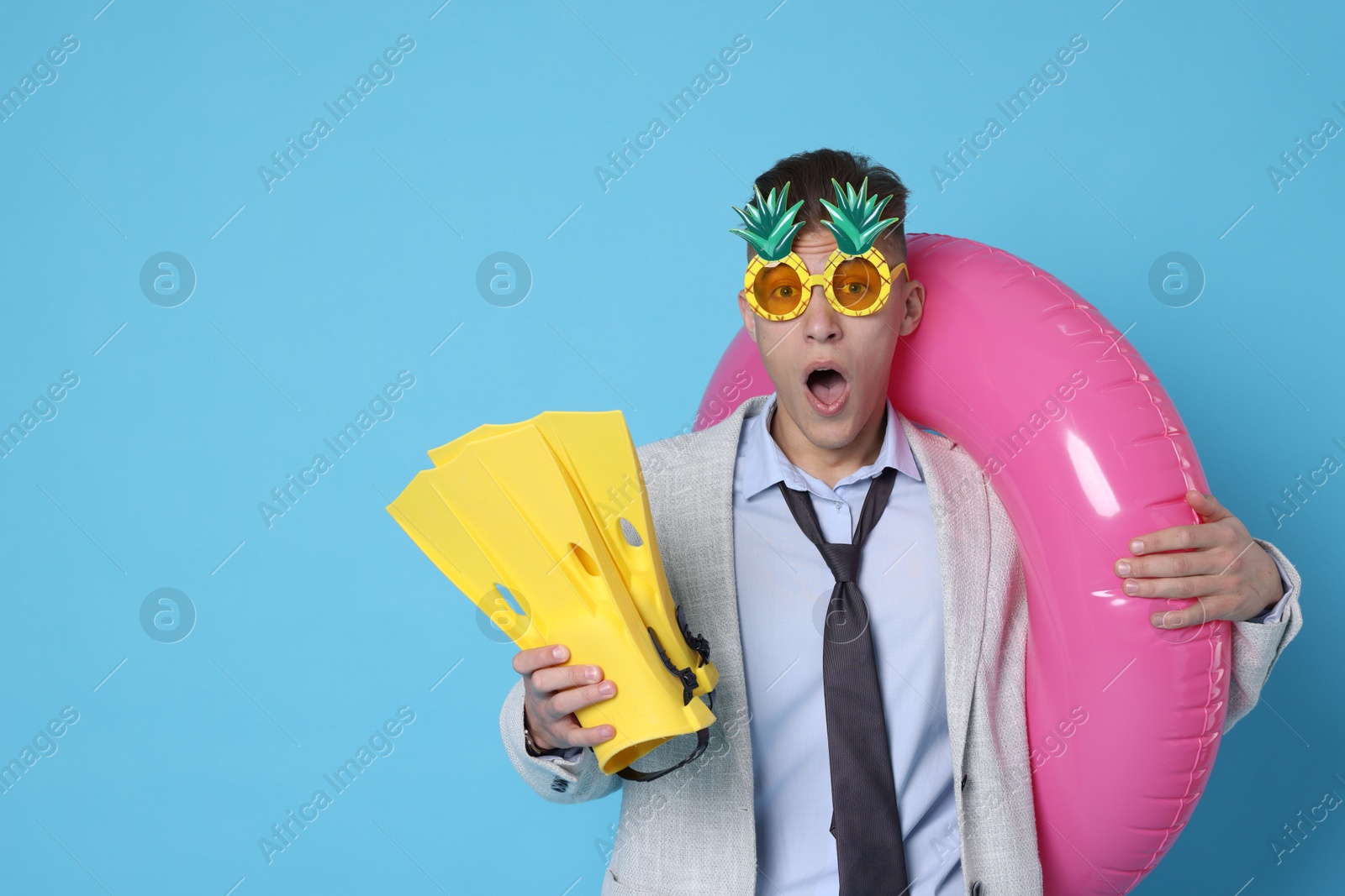 Photo of Businessman with inflatable ring, funny sunglasses and flippers on light blue background, space for text