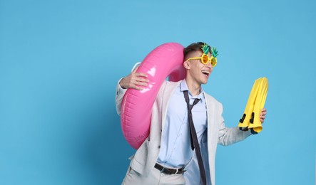 Photo of Businessman with inflatable ring, funny sunglasses and flippers on light blue background, space for text