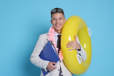 Photo of Businessman with inflatable ring, wreath of flowers and folder on light blue background