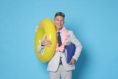 Photo of Businessman with inflatable ring, wreath of flowers and folder on light blue background