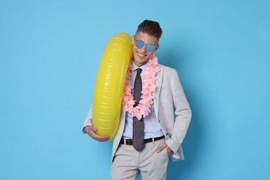 Photo of Businessman with inflatable ring and wreath of flowers on light blue background