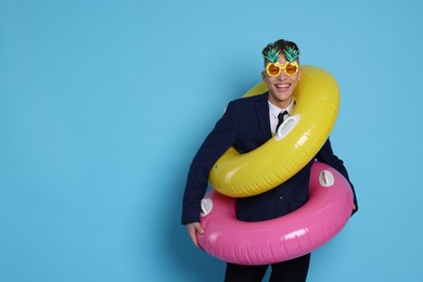 Photo of Businessman with inflatable rings and funny sunglasses on light blue background, space for text