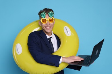 Photo of Businessman with inflatable ring, laptop and funny sunglasses on light blue background