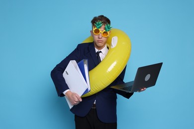 Photo of Businessman with inflatable ring, laptop, folders and funny sunglasses on light blue background