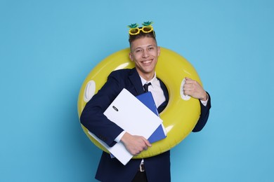 Photo of Businessman with inflatable ring, folders and funny sunglasses on light blue background