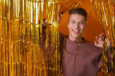 Photo of Happy young man looking out through golden foil curtain against orange background