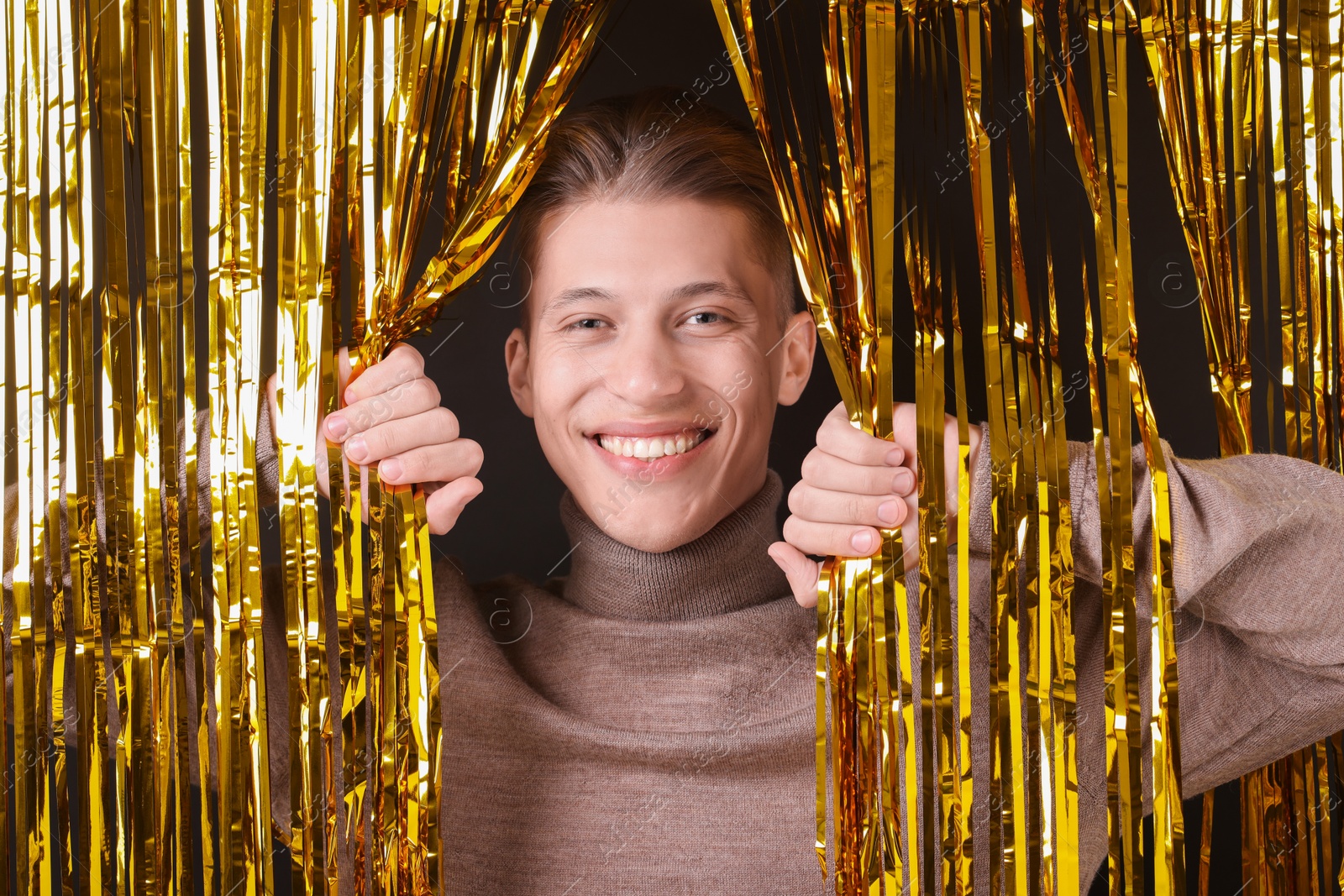 Photo of Happy young man looking out through golden foil curtain against dark background