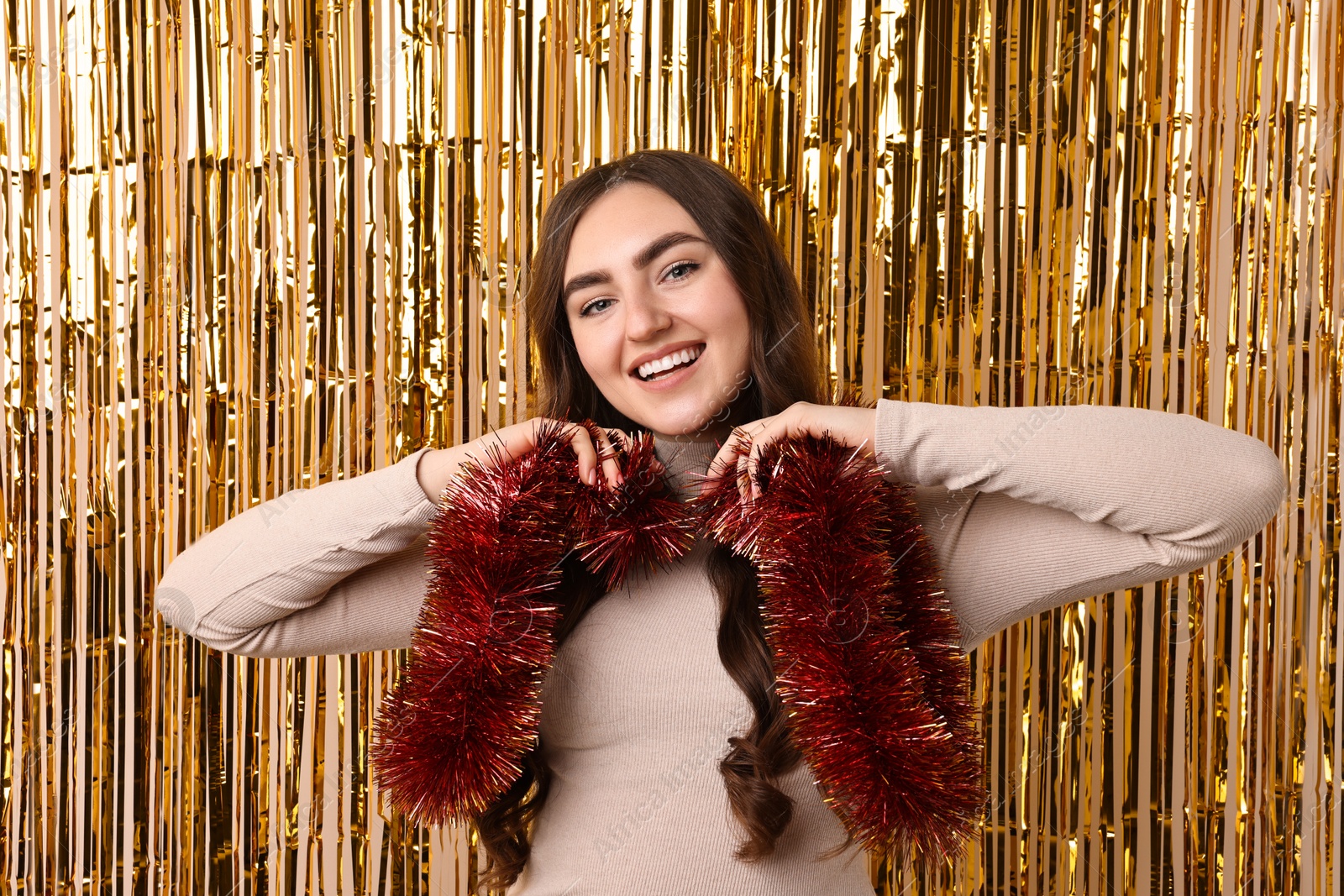 Photo of Happy young woman with tinsel against golden foil curtain