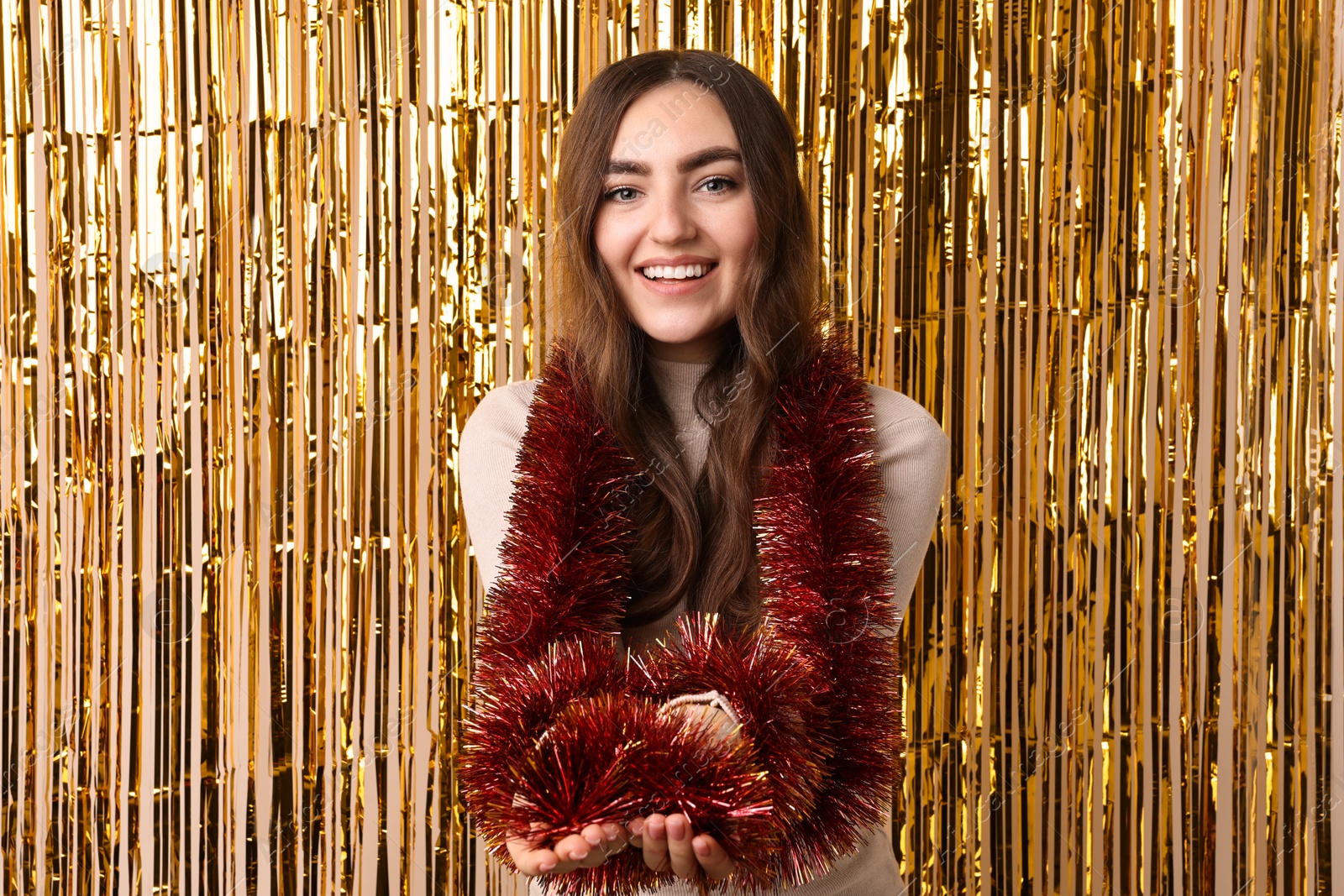 Photo of Happy young woman with tinsel against golden foil curtain