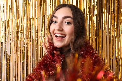 Photo of Happy young woman with tinsel taking selfie against foil curtain