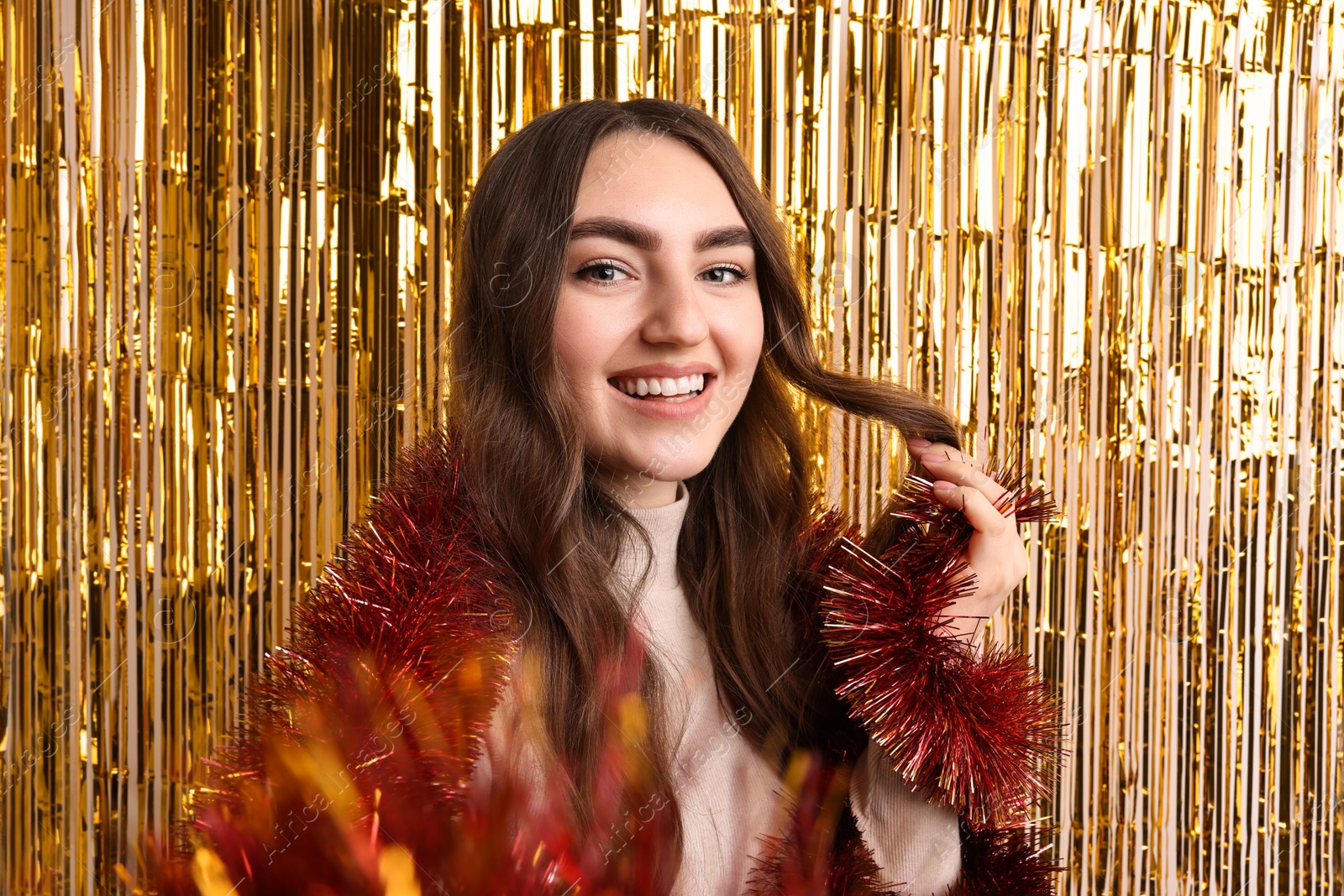 Photo of Happy young woman with tinsel taking selfie against foil curtain