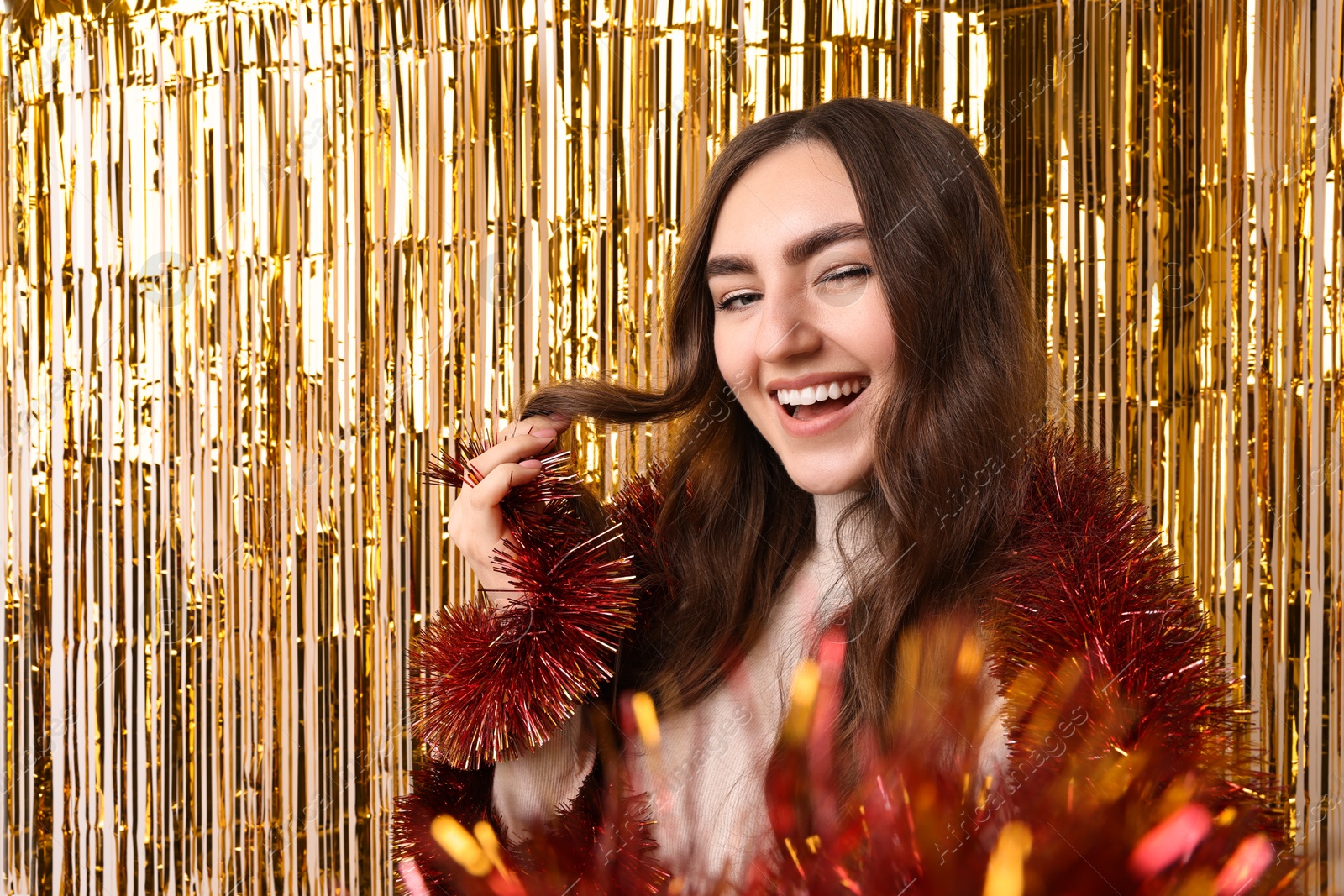 Photo of Happy young woman with tinsel taking selfie against foil curtain