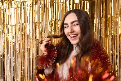 Photo of Happy young woman with tinsel taking selfie against foil curtain