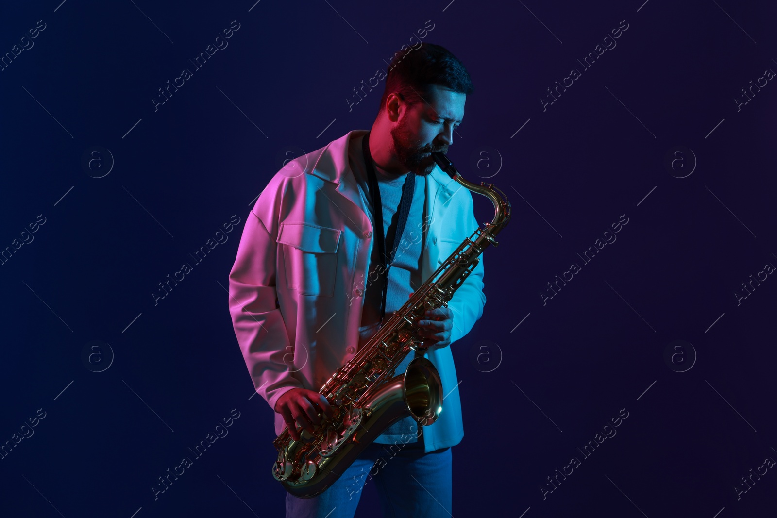 Photo of Professional musician playing saxophone on color background with neon lights