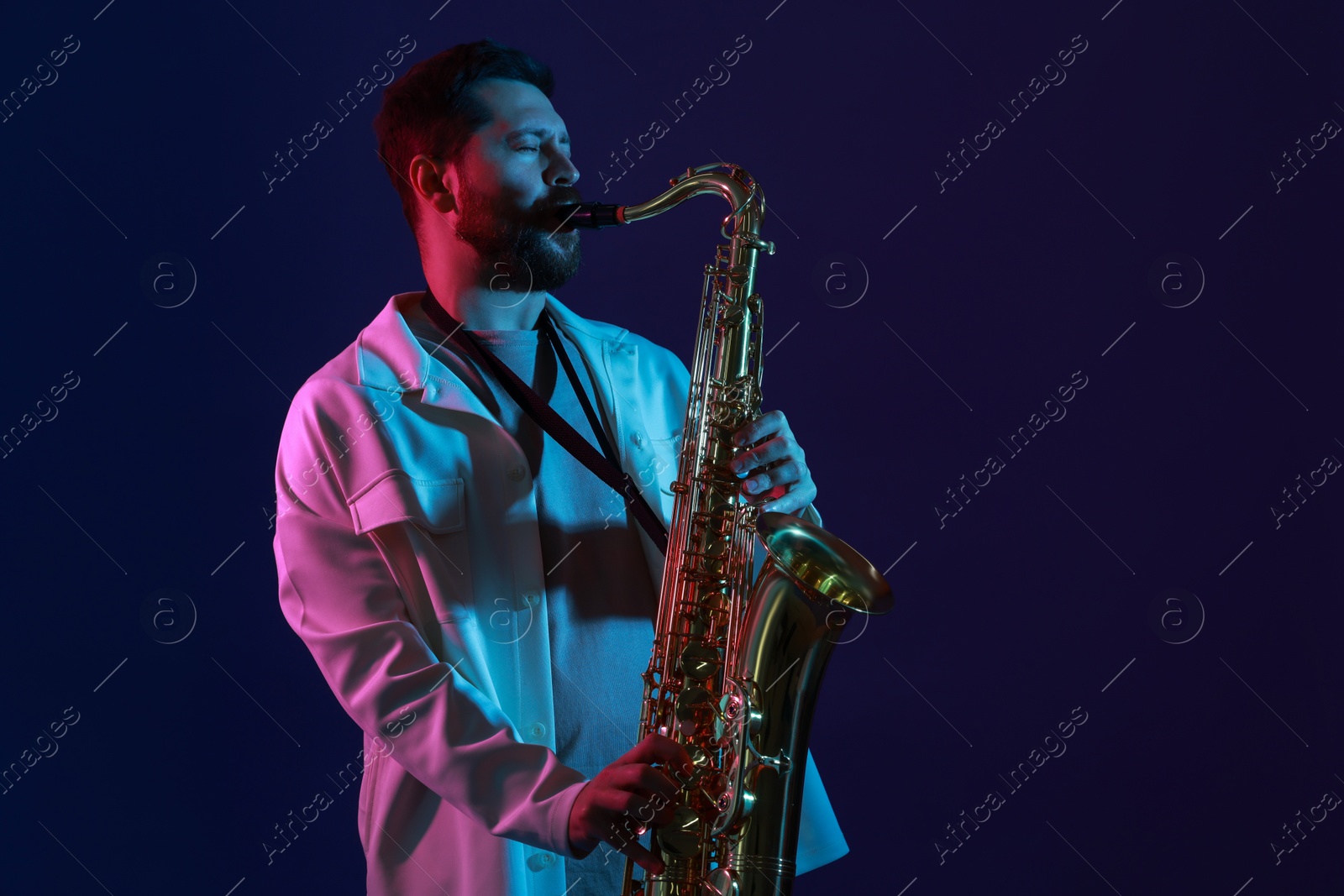 Photo of Professional musician playing saxophone on color background with neon lights. Space for text