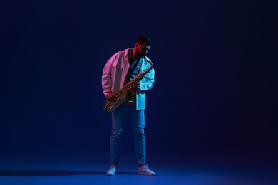 Photo of Professional musician playing saxophone on color background with neon lights