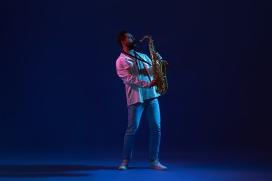 Photo of Professional musician playing saxophone on color background with neon lights