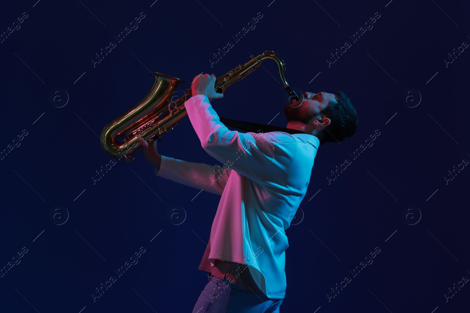 Photo of Professional musician playing saxophone on color background with neon lights