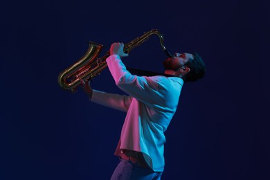 Photo of Professional musician playing saxophone on color background with neon lights