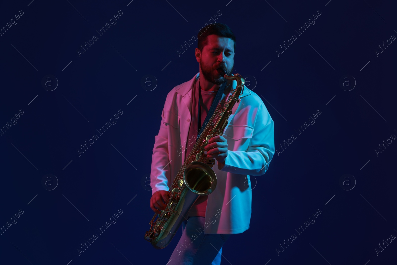 Photo of Professional musician playing saxophone on color background with neon lights