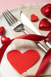 Photo of Romantic place setting for Valentine's day. Cutlery, napkin, plate and decorative hearts on pink wooden table, closeup