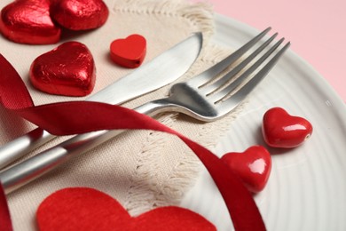 Photo of Romantic place setting for Valentine's day. Cutlery, napkin, plate and decorative hearts on pink wooden table, closeup