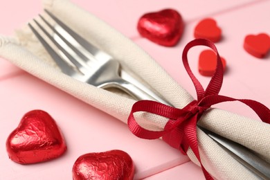 Photo of Romantic place setting for Valentine's day. Cutlery, napkin and decorative hearts on pink wooden table, closeup