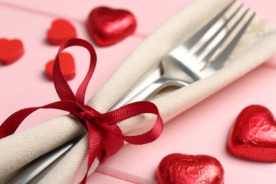 Photo of Romantic place setting for Valentine's day. Cutlery, napkin and decorative hearts on pink wooden table, closeup