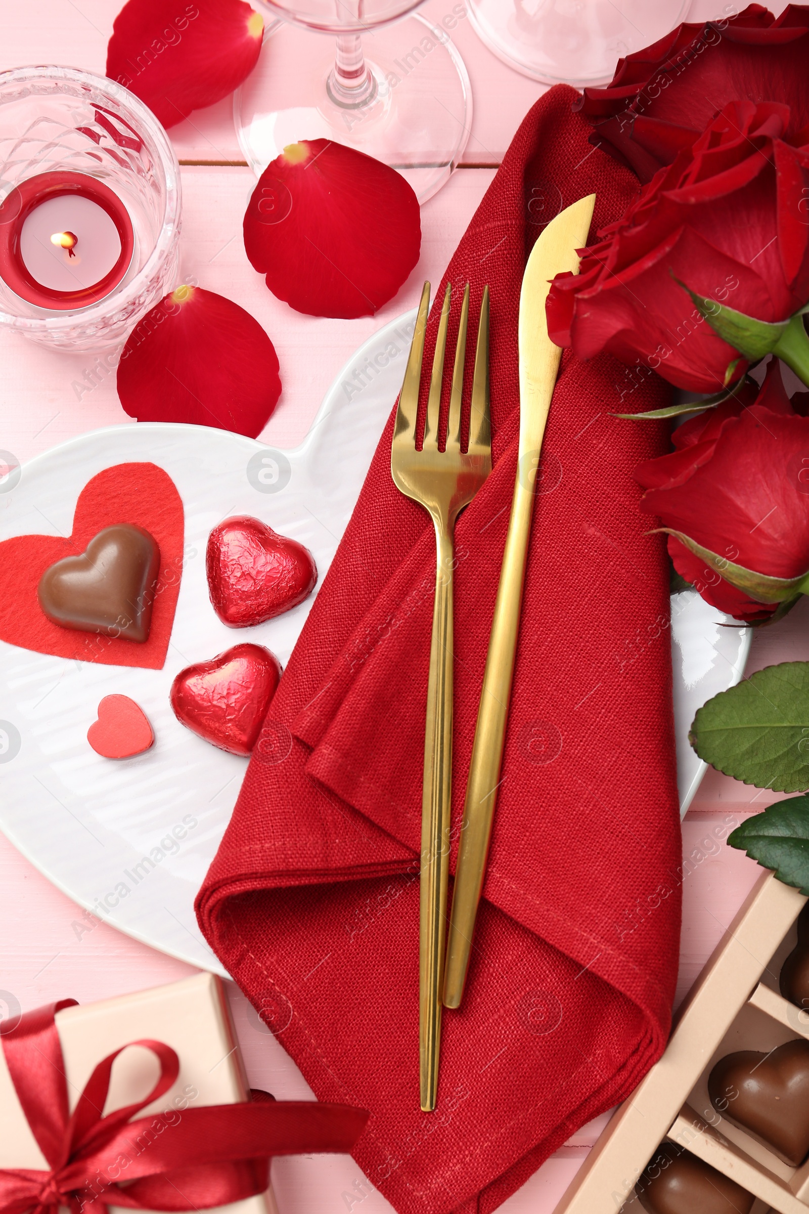 Photo of Romantic place setting for Valentine's day. Cutlery, napkin, plate, roses and decorative hearts on pink wooden table, flat lay