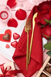 Photo of Romantic place setting for Valentine's day. Cutlery, napkin, plate, roses and decorative hearts on pink wooden table, flat lay