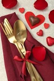 Photo of Romantic place setting for Valentine's day. Cutlery, napkin, candy, petals and decorative hearts on light textured table, flat lay