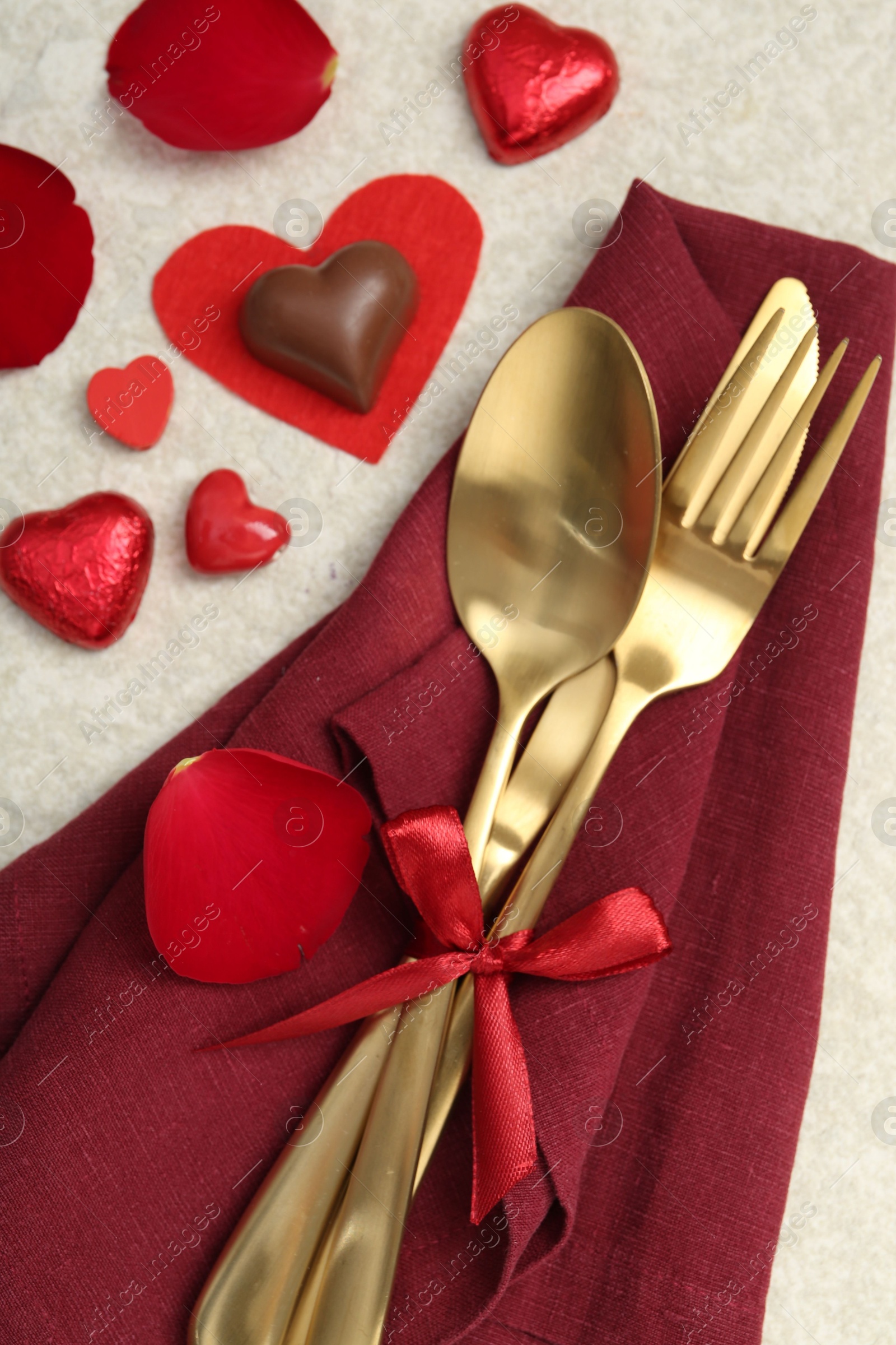 Photo of Romantic place setting for Valentine's day. Cutlery, napkin, candy, petals and decorative hearts on light textured table, flat lay