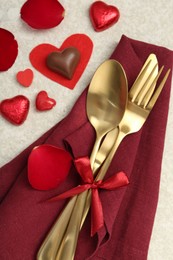 Photo of Romantic place setting for Valentine's day. Cutlery, napkin, candy, petals and decorative hearts on light textured table, flat lay