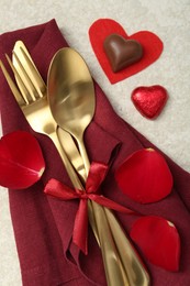 Photo of Romantic place setting for Valentine's day. Cutlery, napkin, candy, petals and decorative hearts on light textured table, flat lay