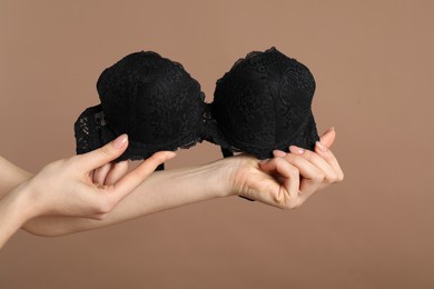 Photo of Woman holding black bra on dark beige background, closeup